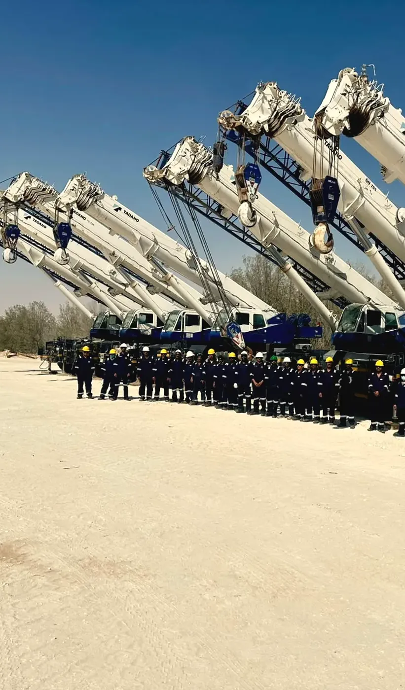 Ajyal rough-terrain cranes with booms raised and the crew lined up beneath