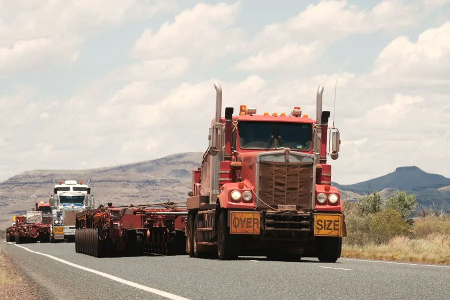 Heavy-haul prime mover with OVERSIZE boards leading a convoy on a desert highway