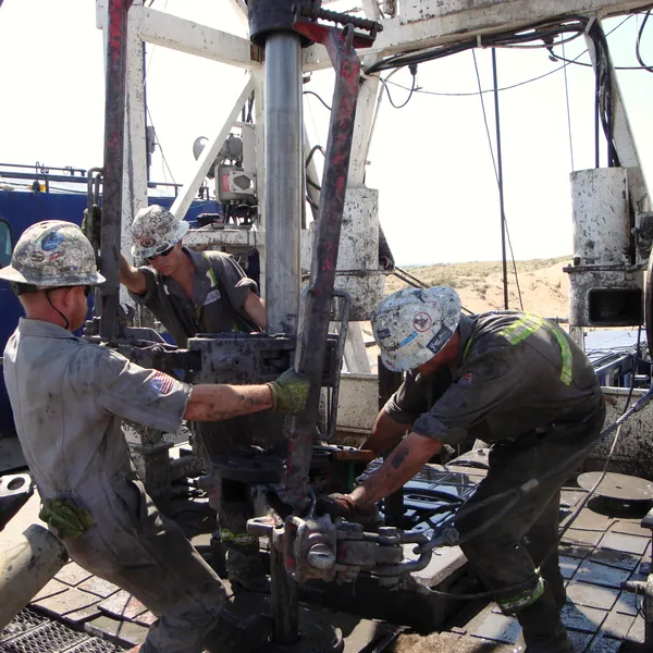 Crew working the tongs at the rotary table on a drilling rig